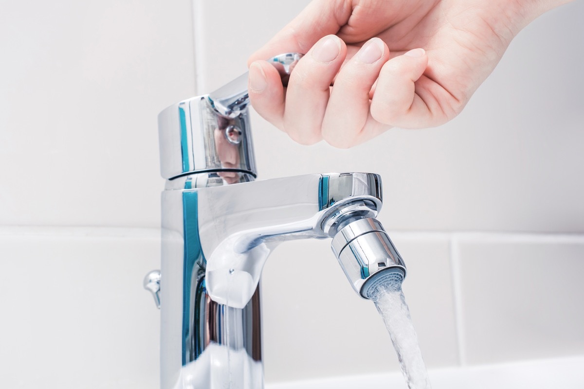 Female Hand On The Handle Of A Chrome Faucet Turned On Water