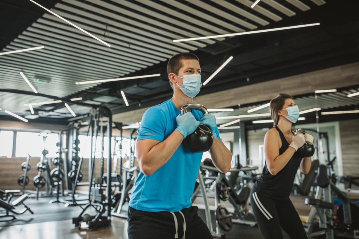 Instructor and student workout at gym after pandemic reopening. They work hard with weights to stay in shape