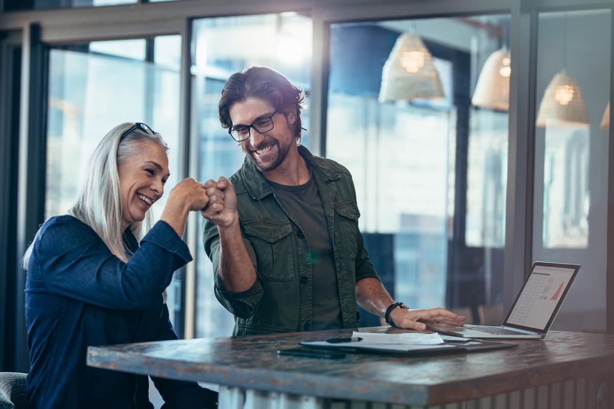 older white woman fist bumping younger white male coworker