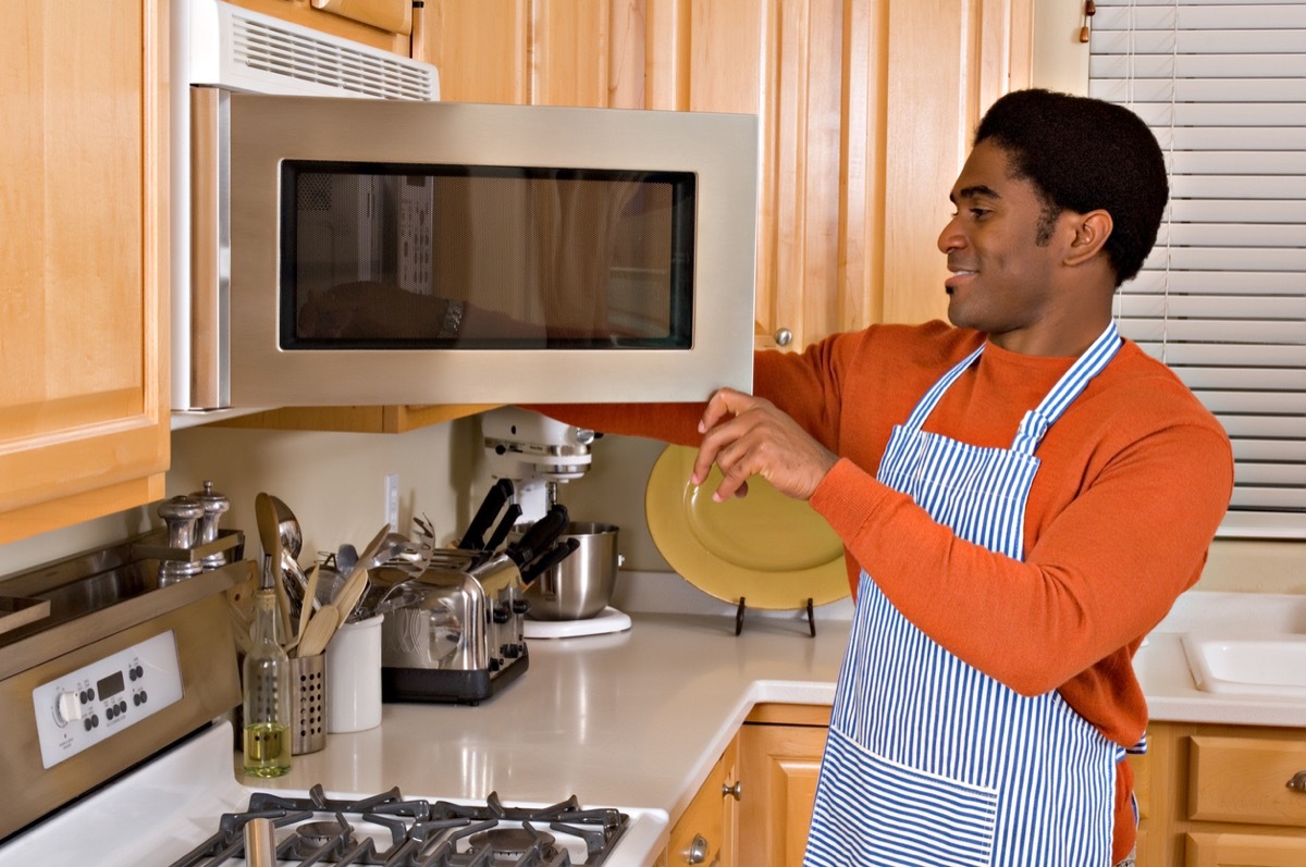  African-American man uses microwave to cook dinner in kitchen