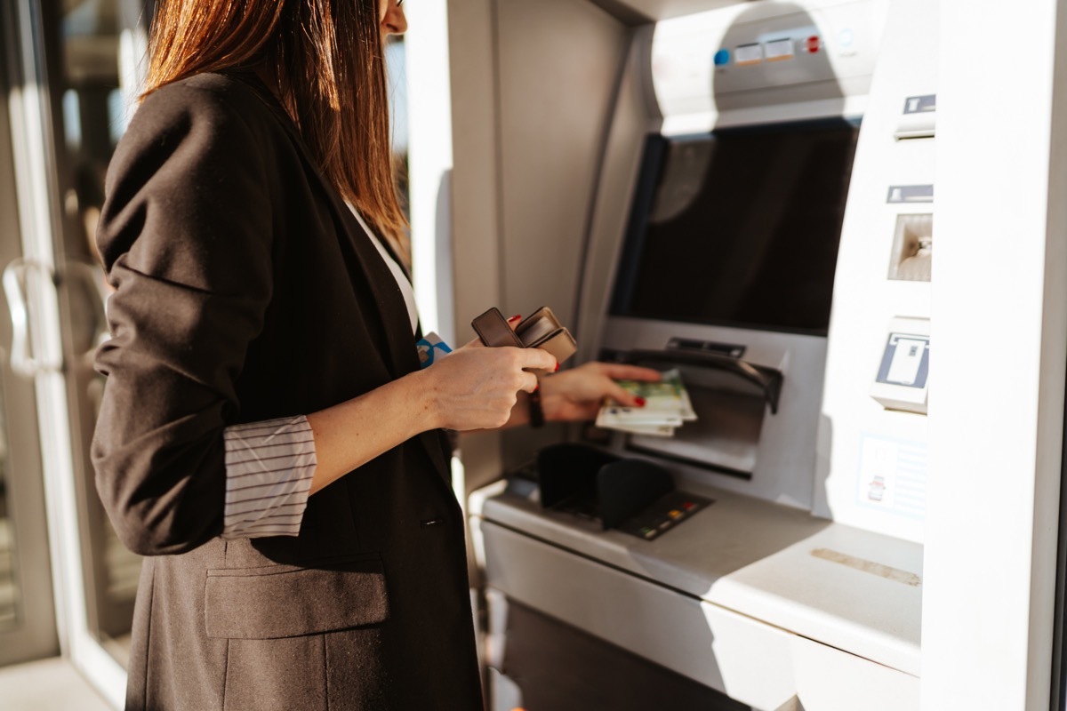 Young woman using outdoor cash machine on sunny spring day