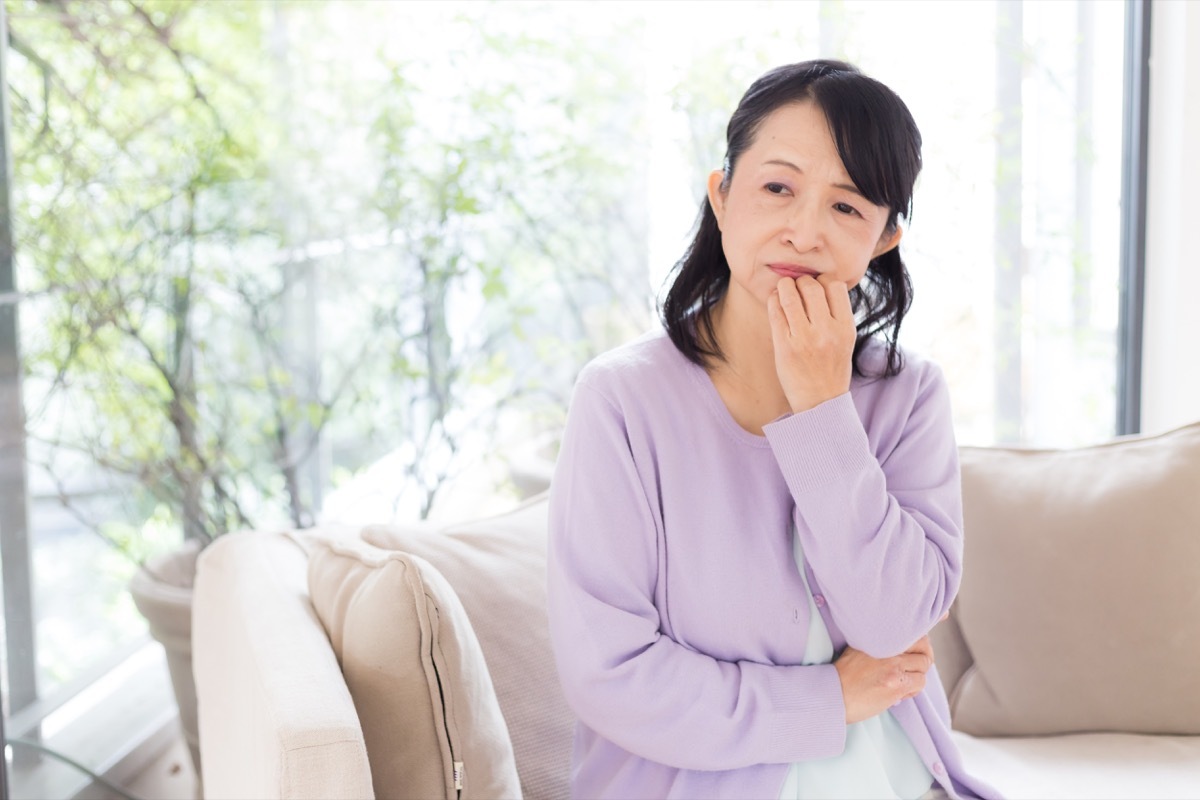 older asian woman looking anxious on the couch