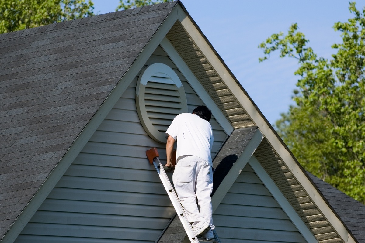 Painter working at the top of an extension ladder on a two story suburban home.