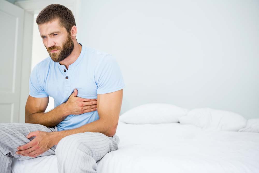 A young man sitting up in bed grabbing his chest with a pained look on his face