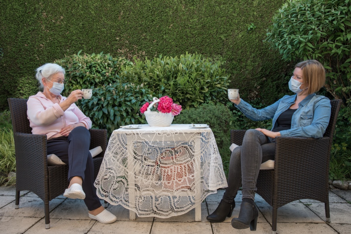 Senior woman and daughter having coffee at safety distance in the garden.