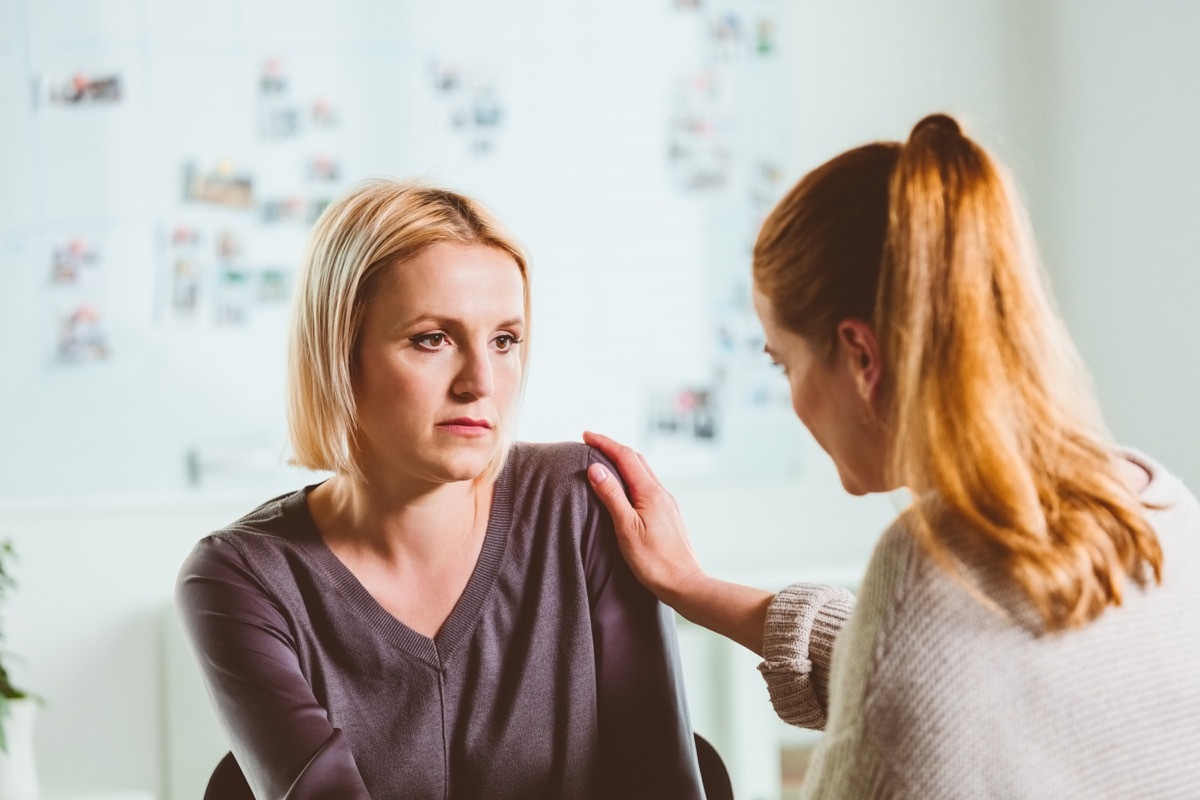 Psychotherapist consoling depressed mid adult woman. Sad female is looking at mental health professional during therapy session. They are sitting in community center.