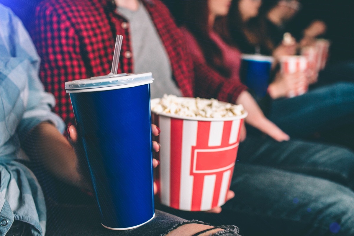 Close up of tasty but unhealthy food. There are basket of popcorn and a blue cup of coke on picture. Man and woman are holding it together