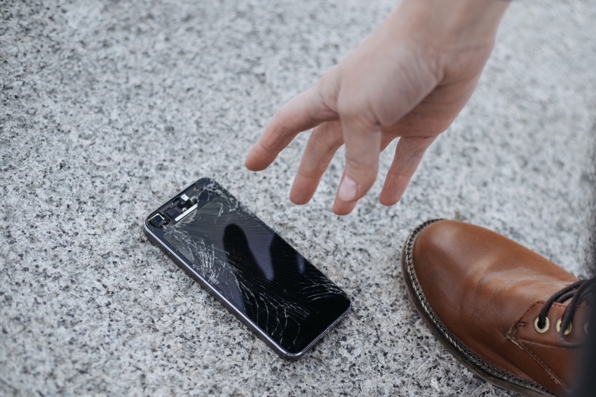 man picking up phone after dropping it on the ground