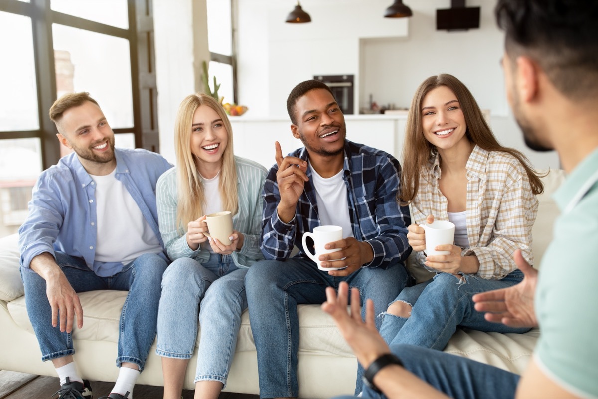 young friends having social gathering, talking and laughing, drinking tea or coffee at home.