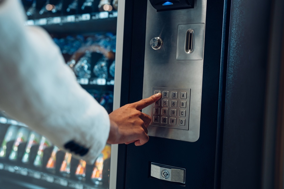 Close up view of woman's finger pushing number button on keyboard of snack vending machine. Self-used technology and consumption concept