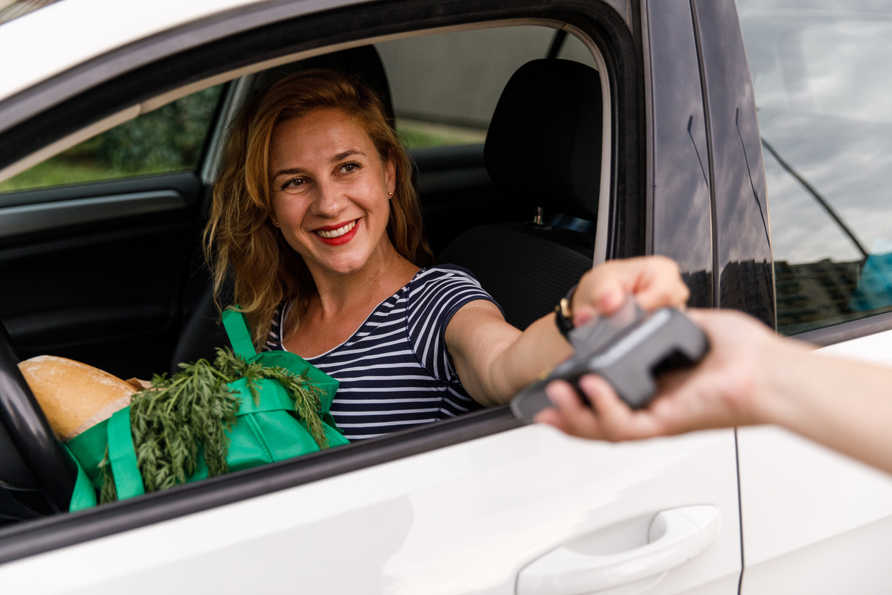 A woman in her car paying for curbside pick up groceries with a credit card