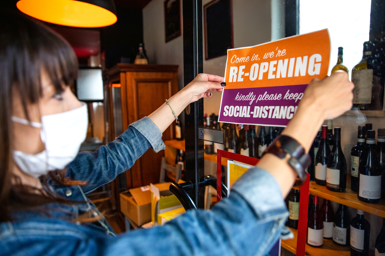 A female shop clerk wearing a face mask putting up a social distancing sign