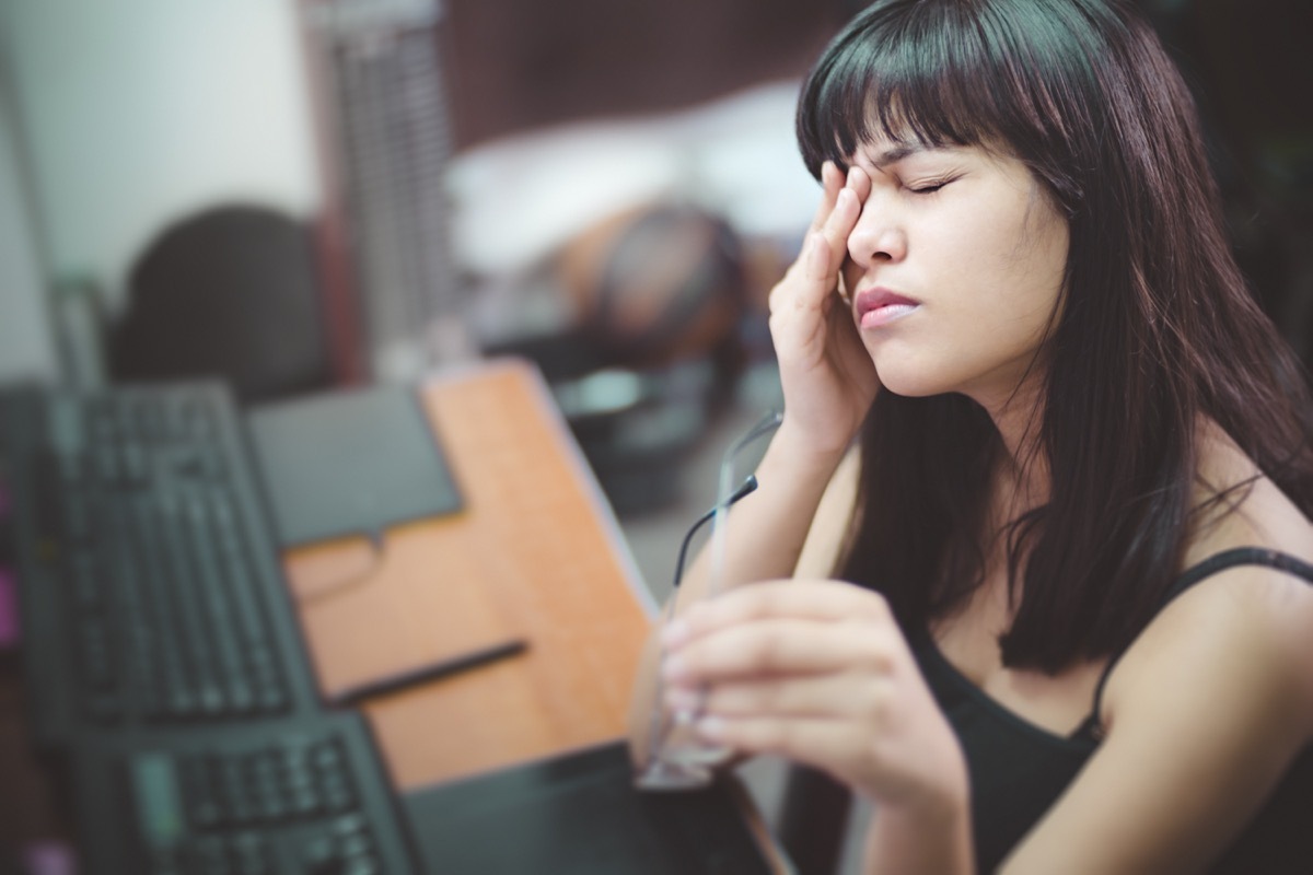 young woman rubbing her eye and holding eyeglasses. She is suffering with aching eyes while working long hours on computer at home.