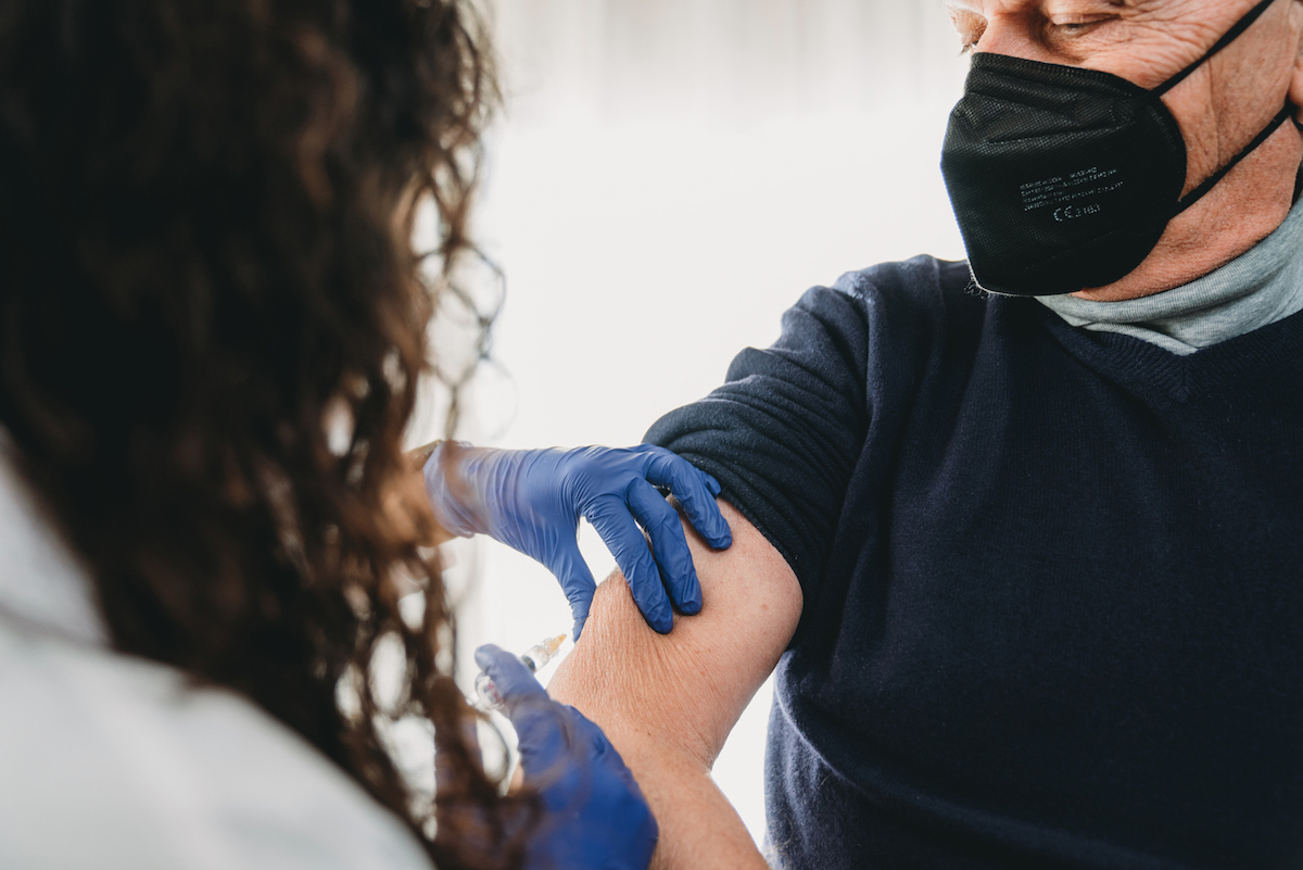 A female doctor is vaccinating a senior man against Covid-19