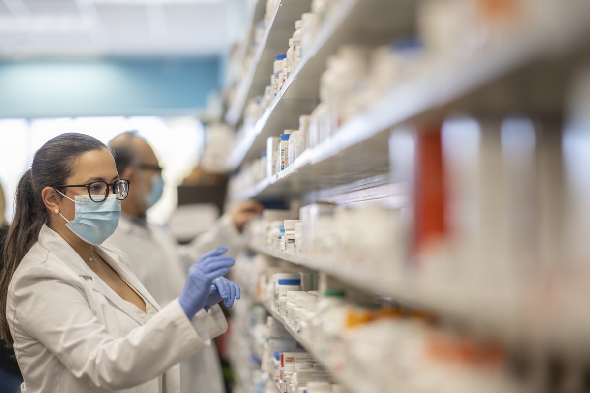 Pharmacist working at a pharmacy organizing products while wearing a protective face mask during the coronavirus outbreak.