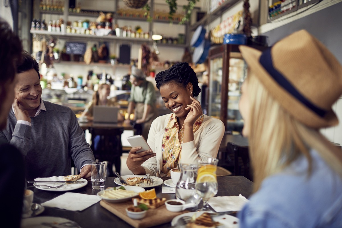 Close up of a group of friends enjoying food at a restaurant and using a mobile phone