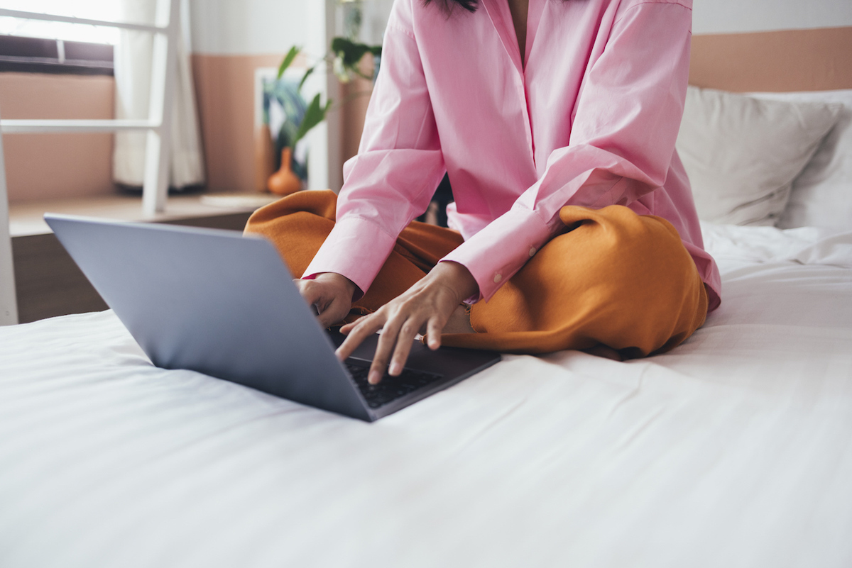 Woman sitting on made bed using laptop