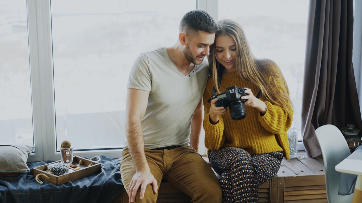 young white man and white woman looking at a camera together sitting by a window in their home