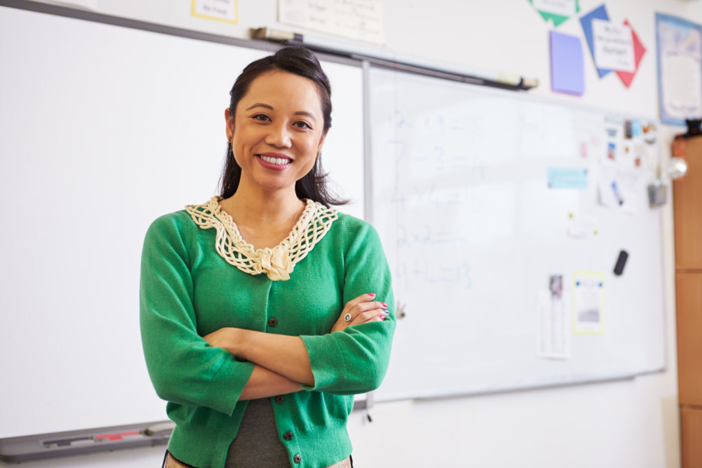 Young female teacher smiling in front of whiteboard in classroom, things you should never say to a teacher