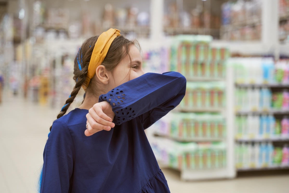 Girl sneezing in store covering with her elbow