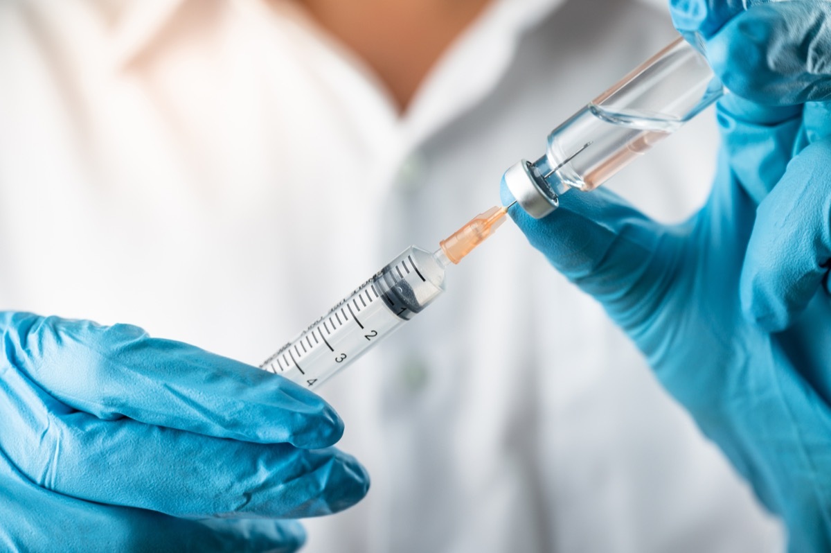 scientist wearing blue gloves holding vaccine vial