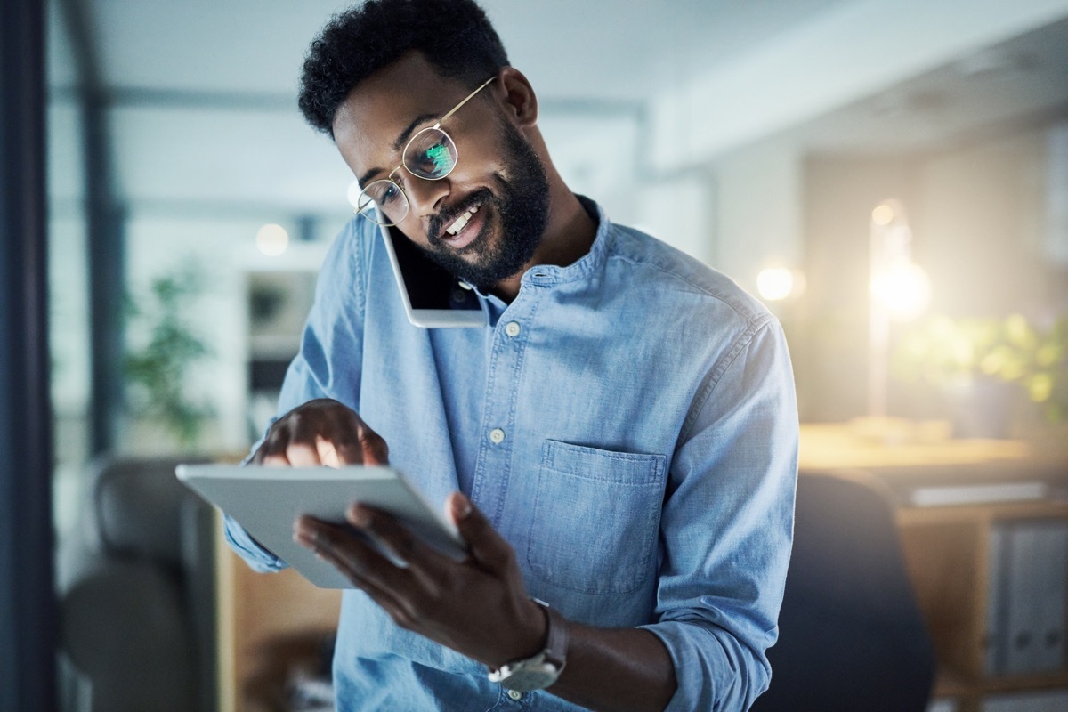 Shot of a young businessman talking on a cellphone while using a digital tablet in an office