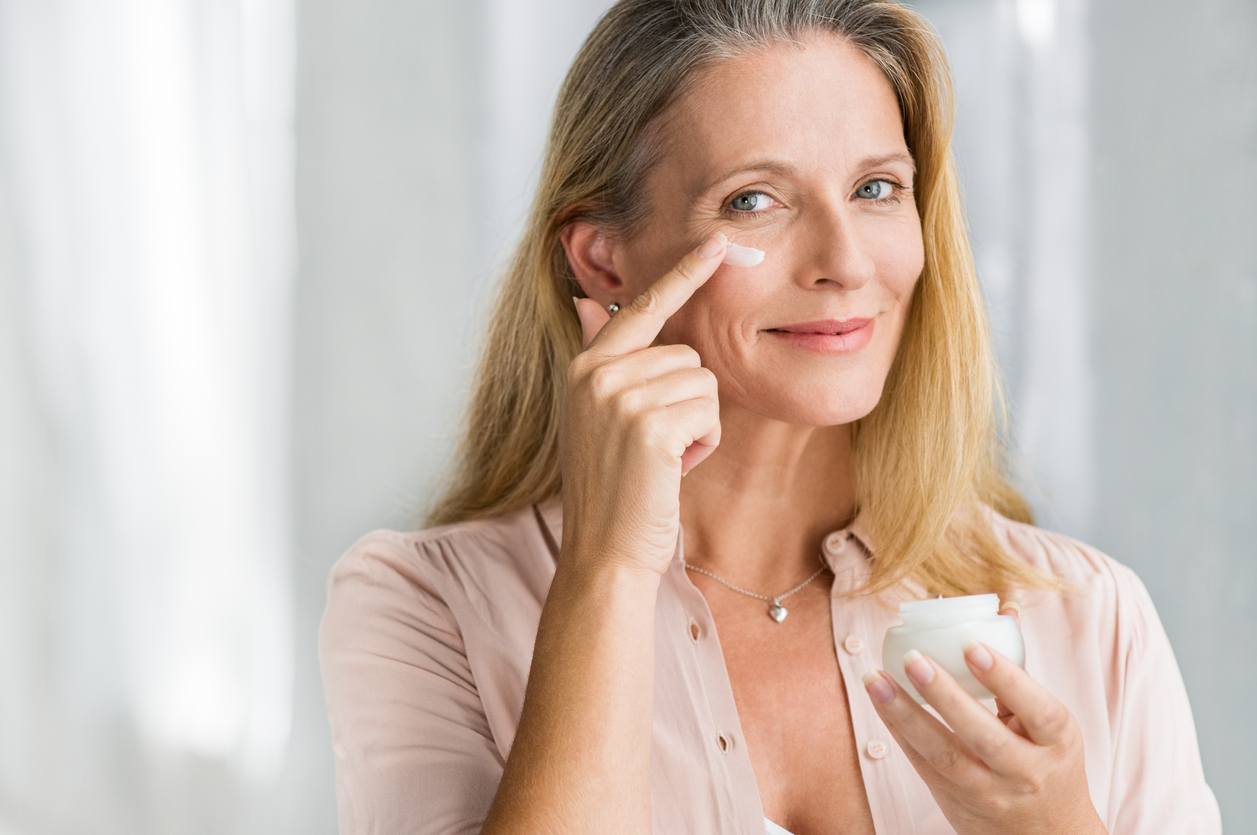 Mature woman applying cream under her eyes.