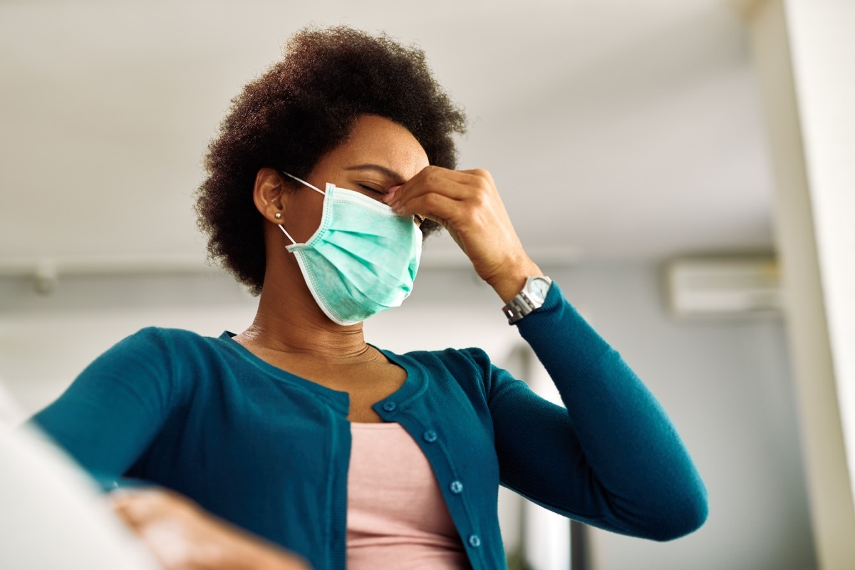 Below view of woman with face mask having a headache at home.