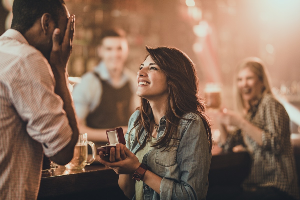 Young happy woman proposing her black boyfriend during night out in a pub. There are people in the background.