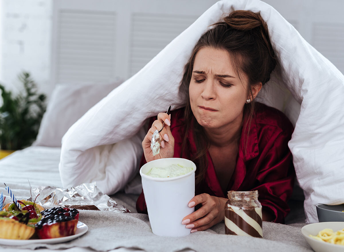 upset woman eating dessert in bed