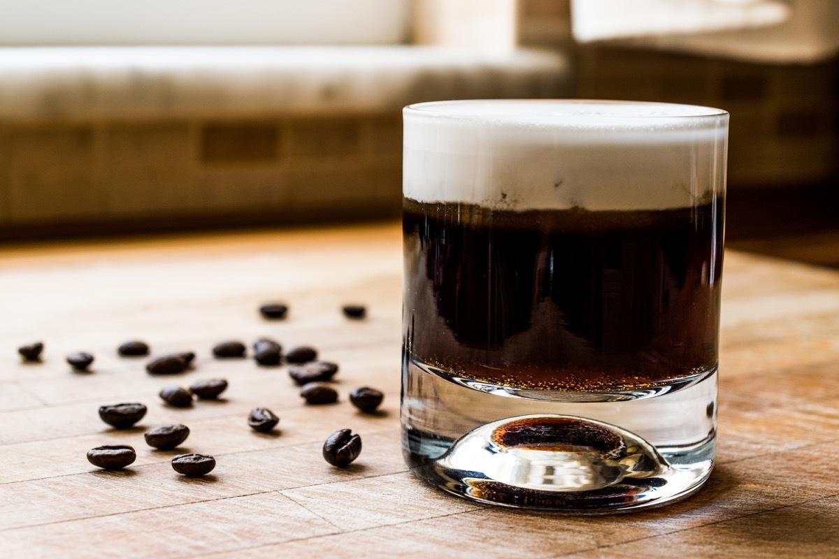 white russian cocktail in glass, on table, alongside coffee beans