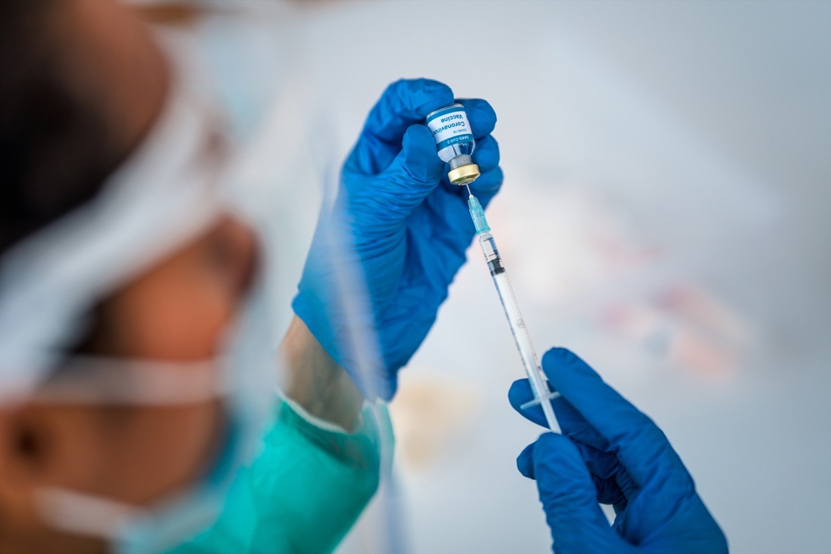 doctor is sitting in a doctor's office and is filling syringe for Covid-19 vaccine