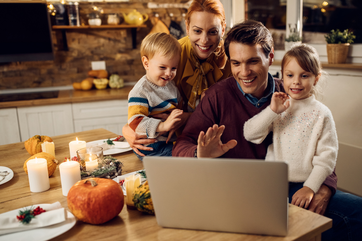 A family of four sits at a Thanksgiving meal while using their laptop to video conference during the COVID pandemic